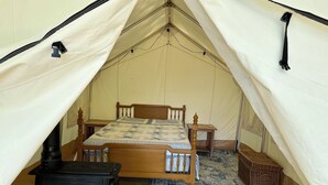 Een tent met een bed, een kleine tafel, een stoel, een fornuis en een vloerkleed.