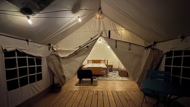 Een tent met een houten vloer, een bed, een stoel en lichtslingers.