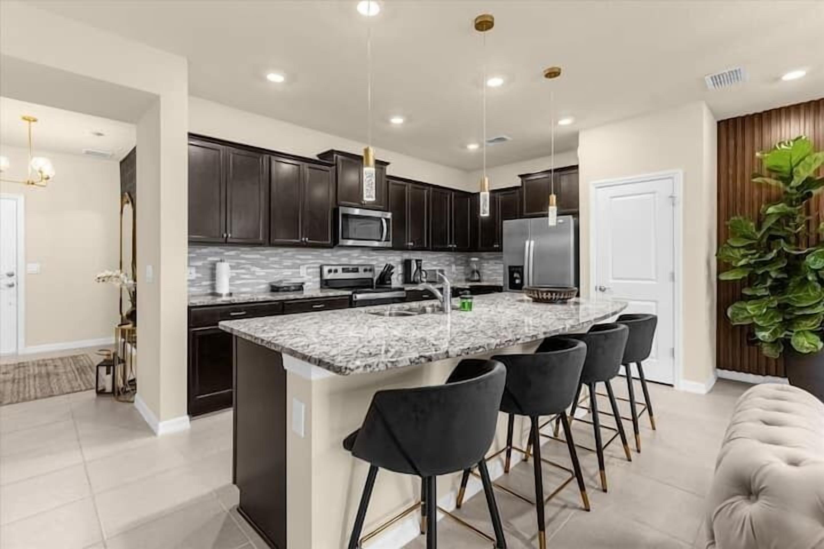 A modern kitchen with dark cabinets, a central island with bar stools, and stainless steel appliances.
