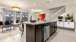 A modern kitchen with a large island, stainless steel appliances, and a staircase leading to another level.