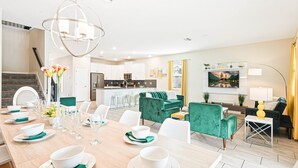 A modern kitchen with white cabinets, a central island, and a dining area with a long table set for six. - Exclusive Champions Gate Retreat w/ Private Pool (Davenport)