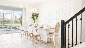 A dining area with a pool view, a white textured wall, and a staircase with black railings. - Exclusive Champions Gate Retreat w/ Private Pool (Davenport)