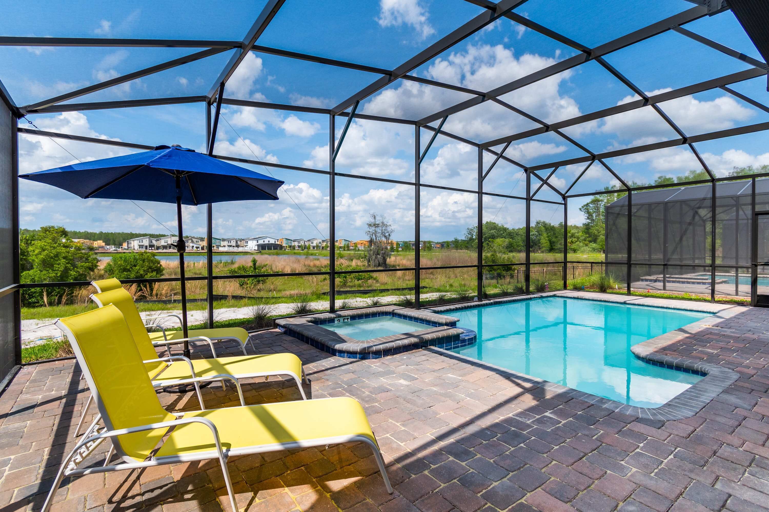 A covered outdoor swimming pool with yellow lounge chairs and a blue umbrella.