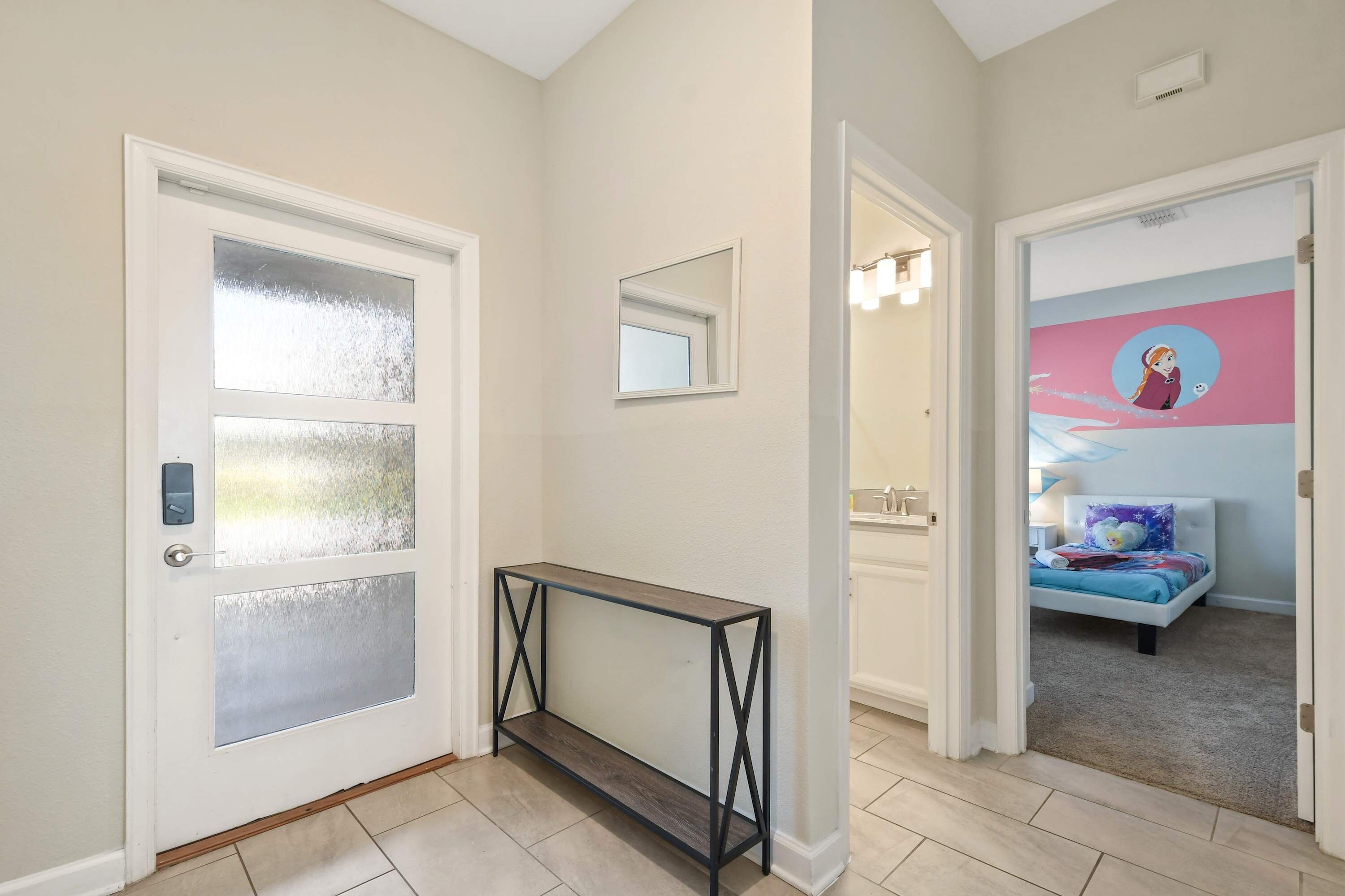 A hallway with a console table, a door with frosted glass panels, and a bedroom with a bed and a wall mural.