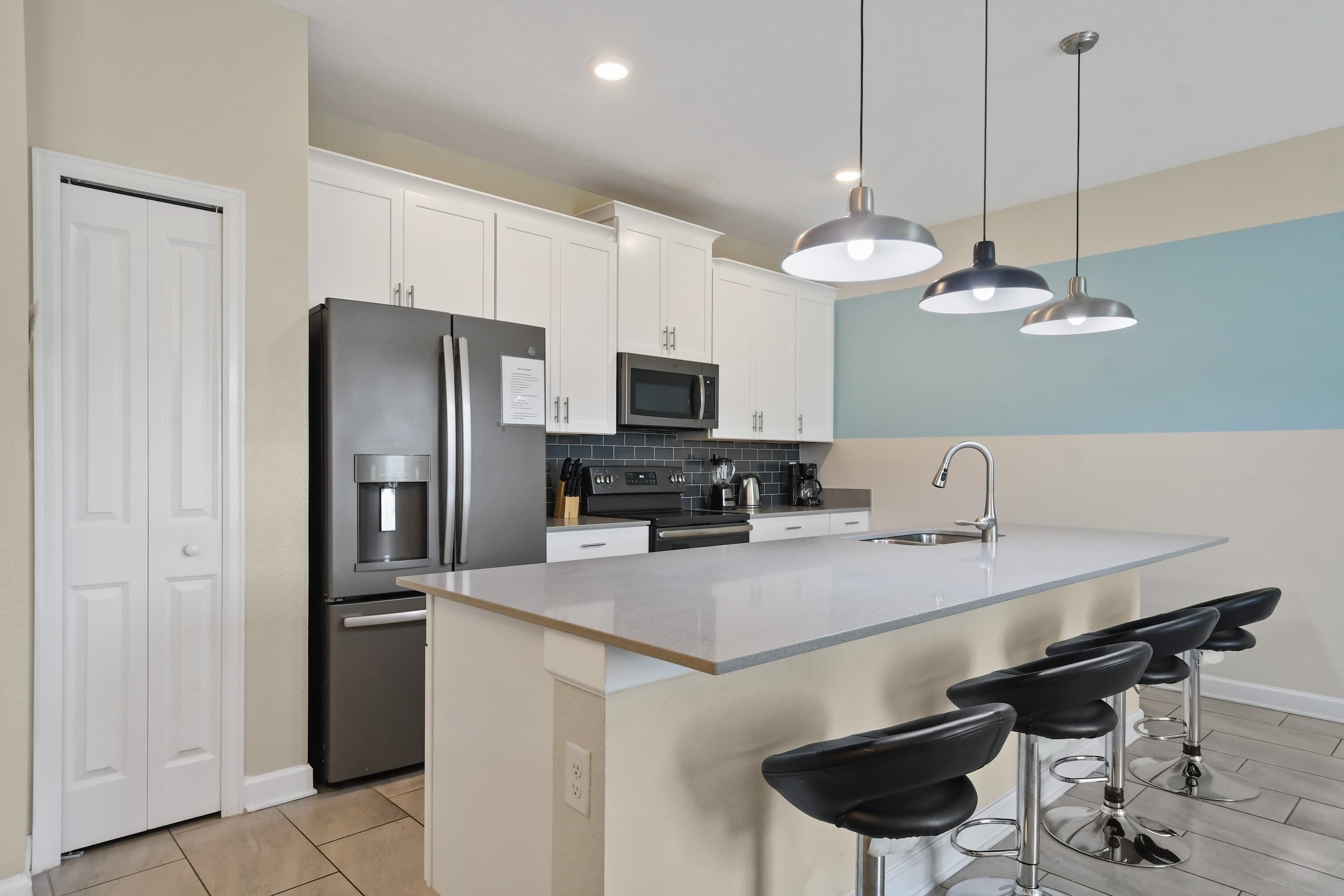 A modern kitchen with white cabinets, stainless steel appliances, a large island with bar stools, and pendant lighting.