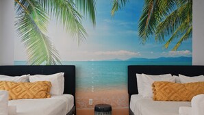 Ein Schlafzimmer mit zwei Betten, einer Wandmalerei von einem Strand und einem Mülleimer.