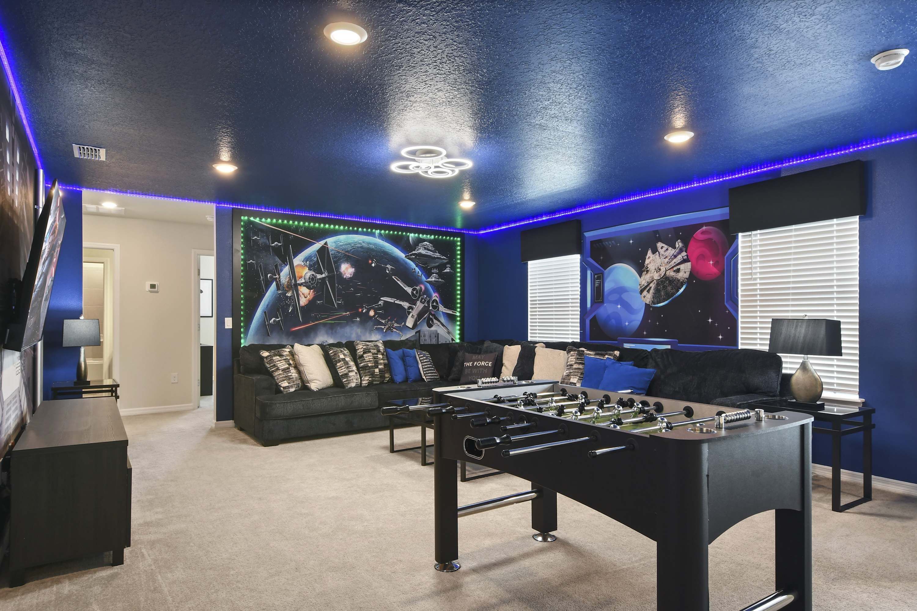A room with a foosball table, a sofa, and Star Wars-themed wall art.