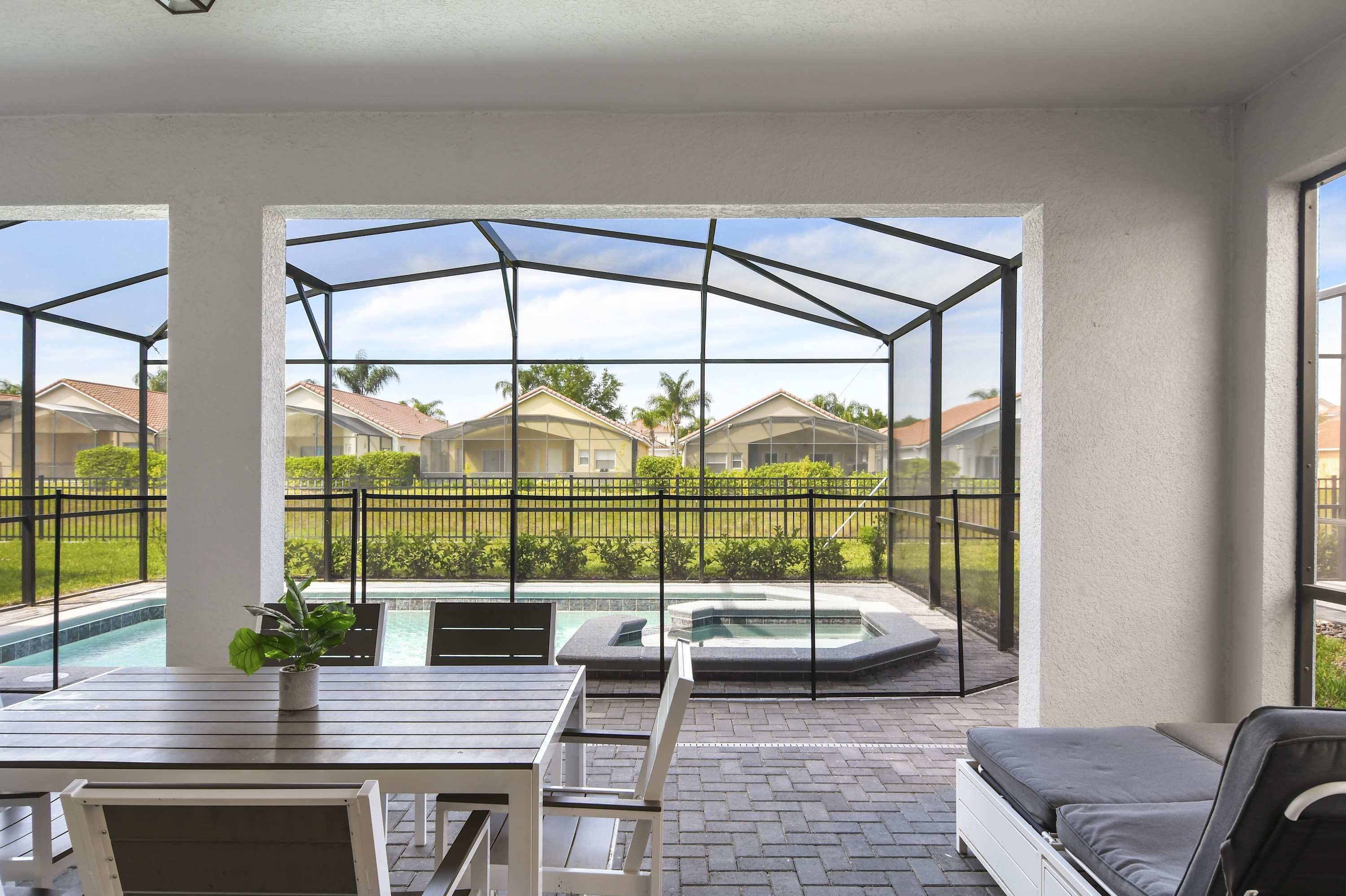 A covered outdoor area with a pool and hot tub, surrounded by a fence, and overlooking a residential neighborhood.