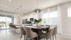 A modern kitchen with white cabinets, a central island, and a dining area with a large table and chairs. - Solterra Resort 5br W/pool Spa New Disney! (Davenport)