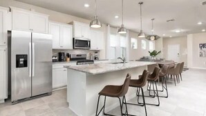 A modern kitchen with white cabinets, stainless steel appliances, and a central island with bar stools. - Solterra Resort 5br W/pool Spa New Disney! (Davenport)