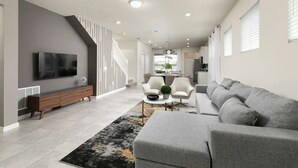 A modern living room with a grey sofa, a flat-screen TV, a wooden console, and a staircase. - Solterra Resort 5br W/pool Spa New Disney! (Davenport)