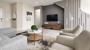 A modern living room with a grey sofa, a round coffee table, and a TV mounted on a grey wall. - Solterra Resort 5br W/pool Spa New Disney! (Davenport)