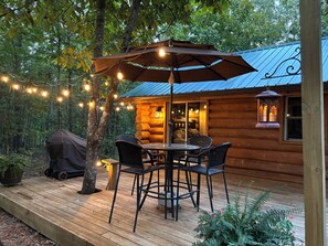 Una cabaña de madera con terraza, mobiliario exterior e iluminación con luces colgantes.