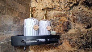 A black metal shelf with two bottles of body wash and shampoo hanging on a stone wall. - Casa de la Villa (Villa de Leyva)