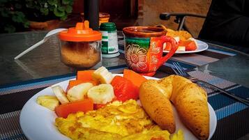 Une assiette de petit-déjeuner contenant des œufs, des bananes, des carottes et des croissants, posée sur une table recouverte d’un set de table.