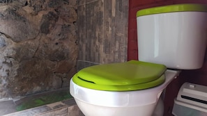Et toilet med grønt låg i et badeværelse med stenvægge og flisegulv.