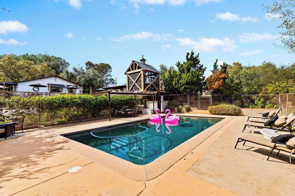 A swimming pool with lounge chairs, a wooden gazebo, and a fenced garden area.