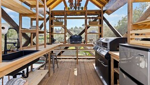 Una terraza de madera con una parrilla, un lavamanos y mesas de madera.