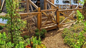 Una cabaña de madera con balcón, rodeada de plantas y un jardín.