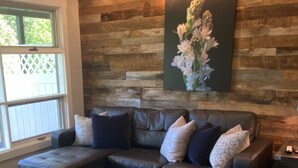 A living room with a sectional sofa and ottoman, a wooden accent wall, and a framed floral artwork. - Gorgeous serene lake and beach front hide away (Flat Rock)