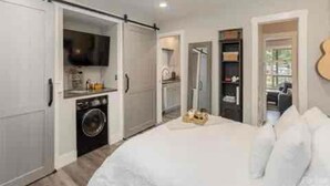 A compact bedroom with a bed, a washing machine, and a television in a small kitchenette area. - Gorgeous serene lake and beach front hide away (Flat Rock)
