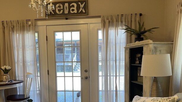 A cozy living room with a beige sofa, a small table with a chair, a chandelier, and a sign that reads "Relax".
