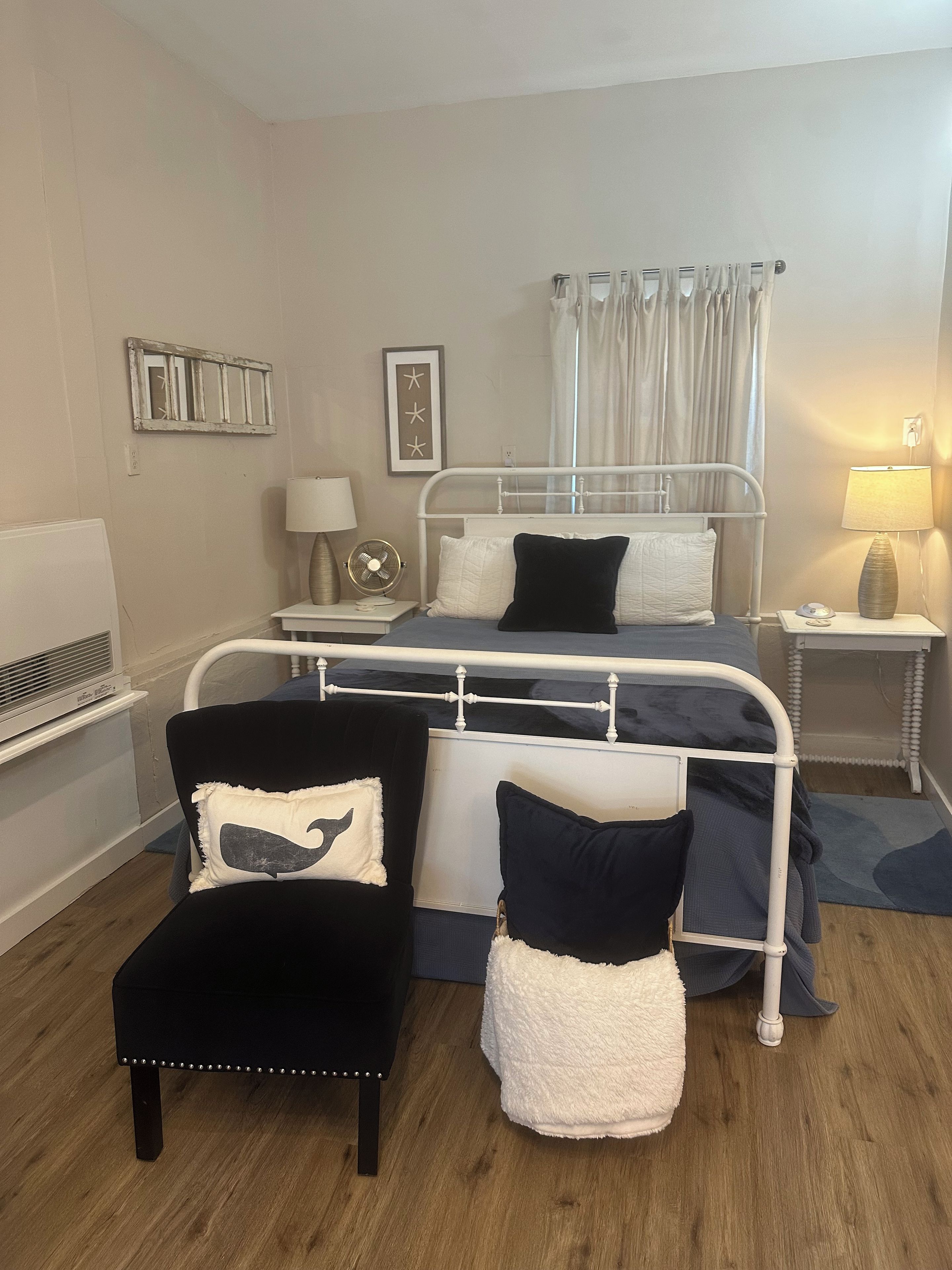 Een slaapkamer met een bed, een stoel, een nachtkastje, een lamp en een ventilator bevestigd aan de muur.
