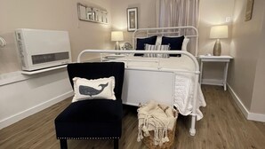 Un dormitorio con cama, una silla, una mesita de noche, una lámpara y un aire acondicionado instalado en la pared.