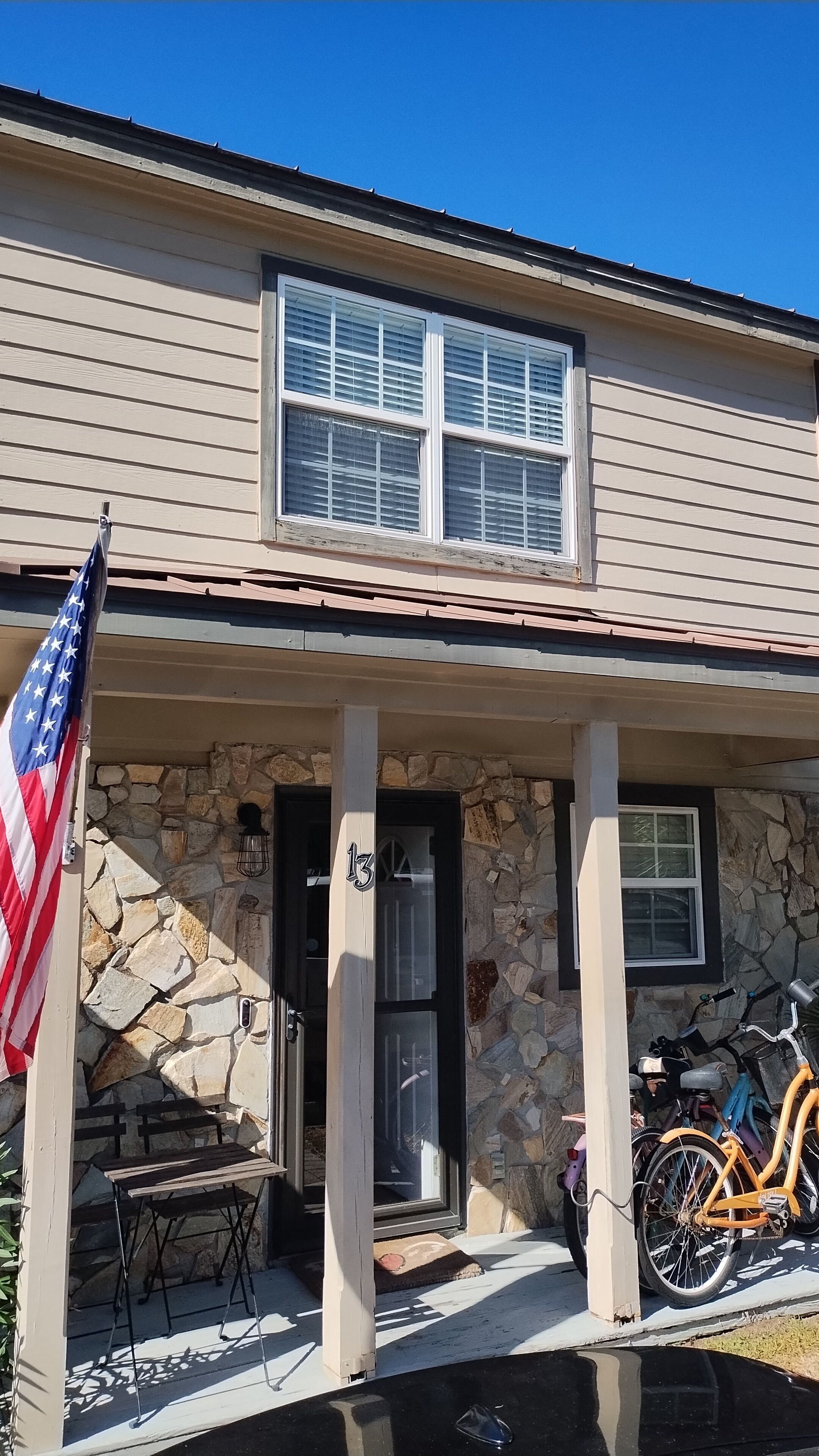 Een huis met een stenen gevel, een voortuin en een Amerikaanse vlag, met een fiets die ervoor geparkeerd staat.