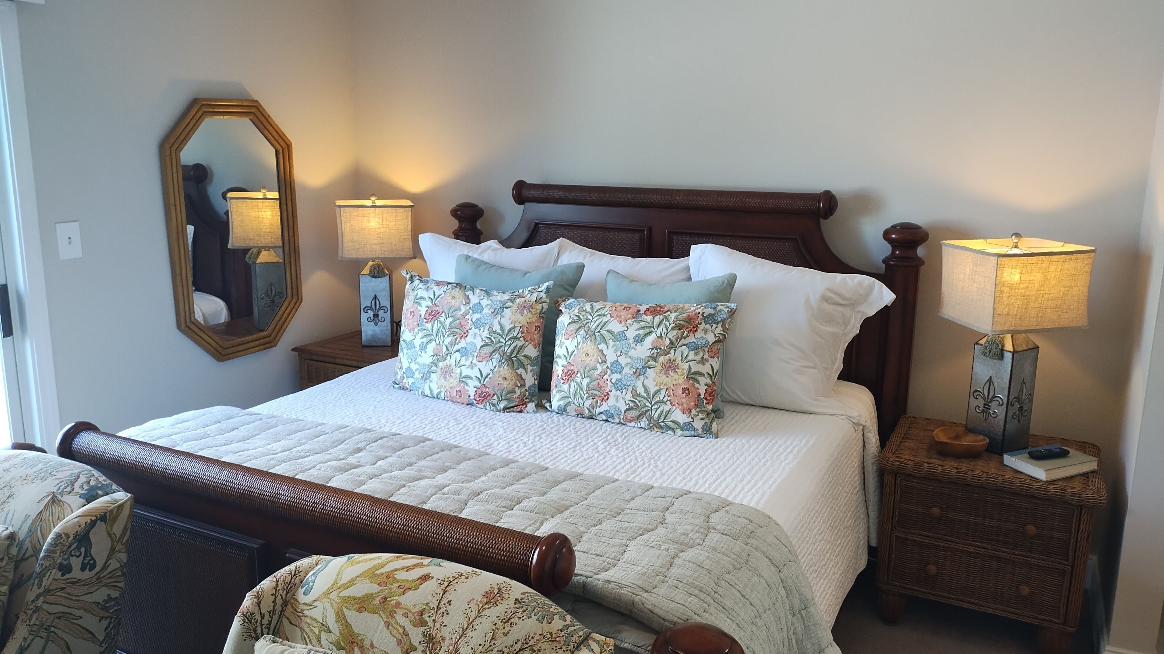 A neatly made bed with floral pillows, a wooden headboard, two bedside tables with lamps, and a mirror on the wall.