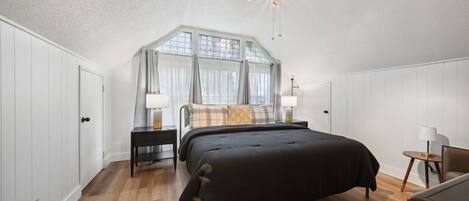 Une chambre avec un grand lit, un ventilateur de plafond, une fenêtre avec des rideaux et une table de chevet avec une lampe.