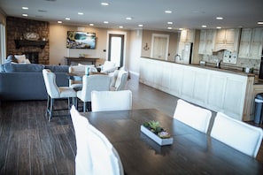 A modern living room with a fireplace, a dining area with a wooden table, and a kitchen with white cabinets.