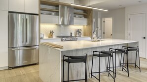 A modern kitchen with a large island, stainless steel appliances, and black bar stools. - 201 Verbier Building 4 (Mont-Tremblant)