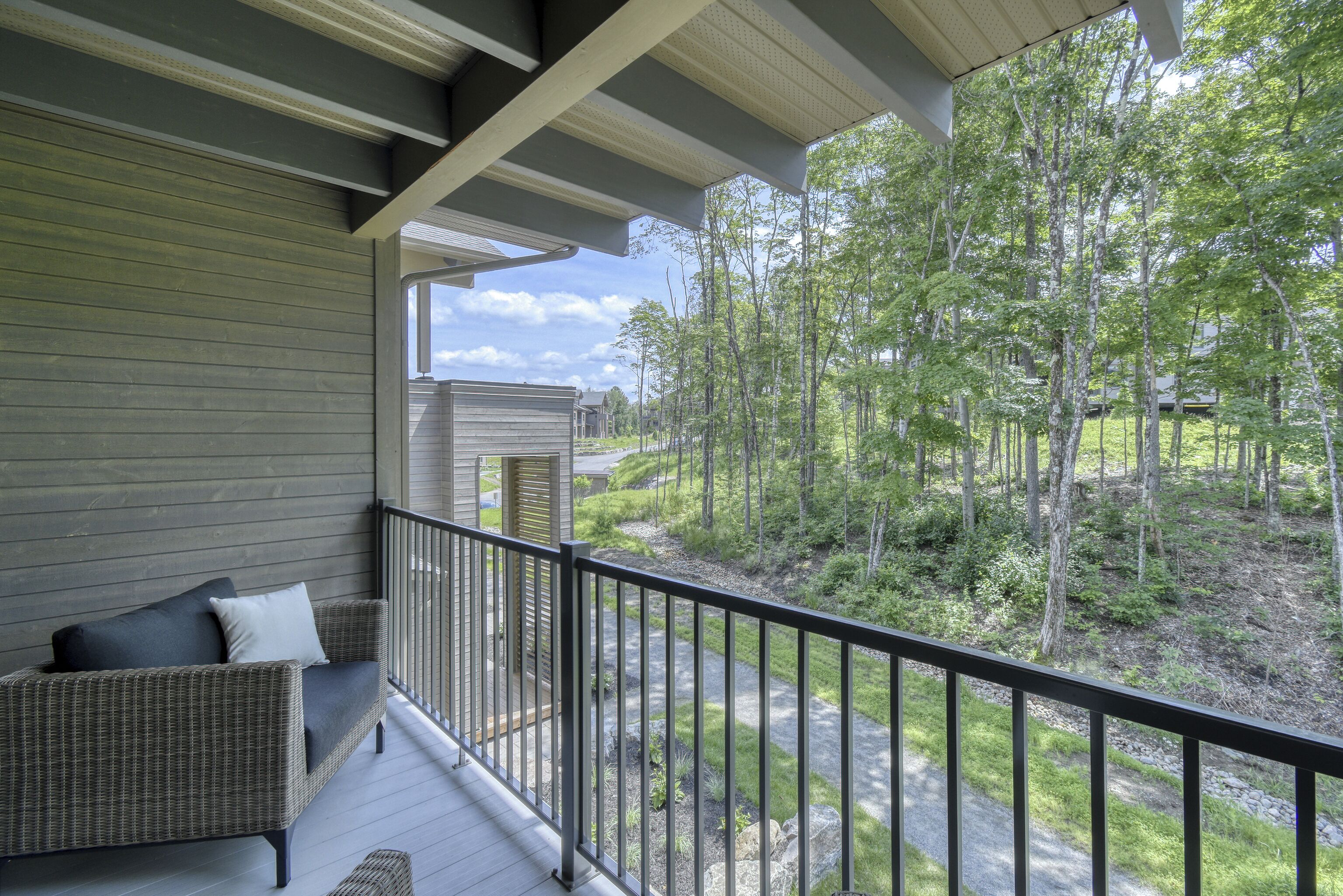 A balcony with a wicker sofa and a view of a forested area.