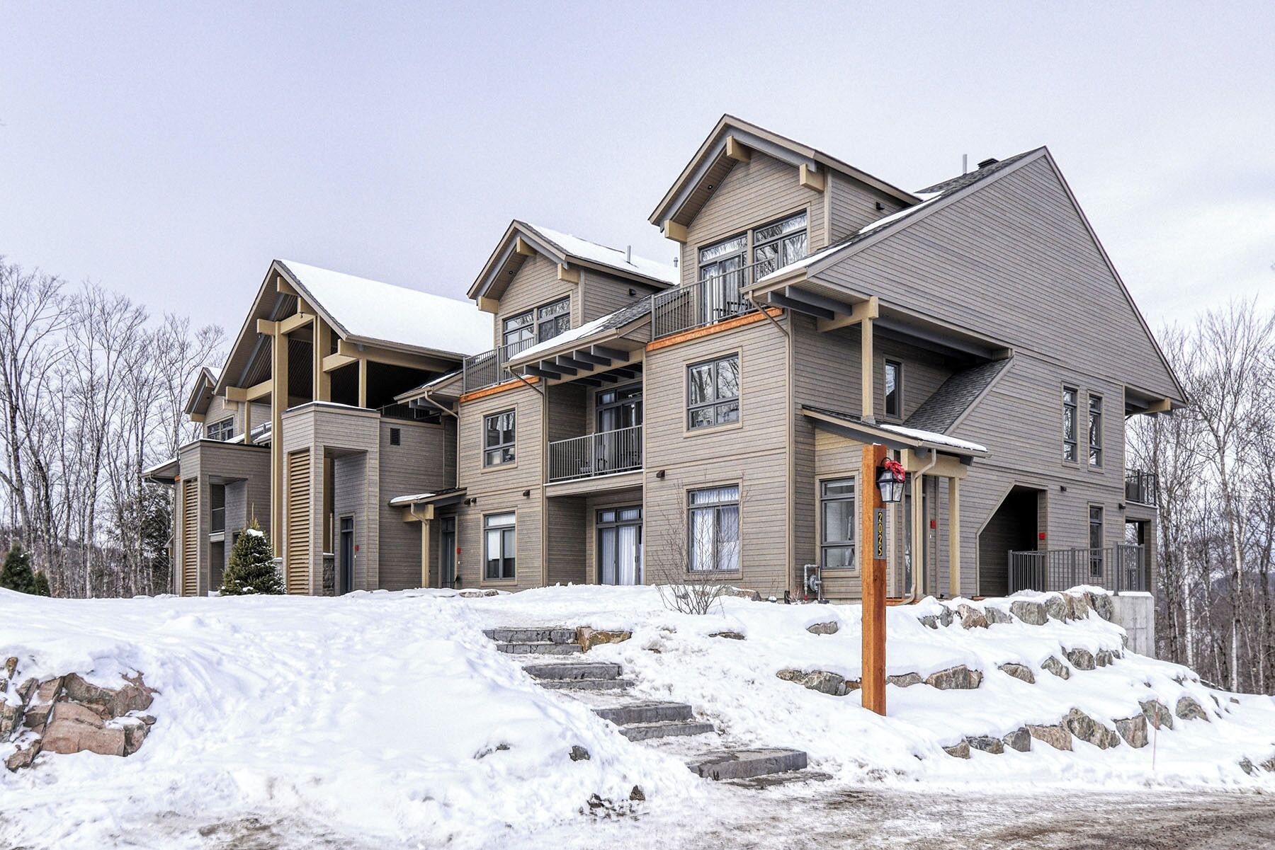A multi-story residential building with a sloped roof, large windows, and a stone staircase leading to the entrance.