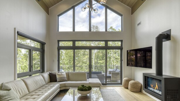 A spacious living room with a large sectional sofa, a fireplace, and large windows offering a view of the outdoors. - 201 Verbier Building 4 (Mont-Tremblant)