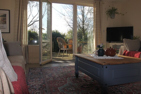 A living room with a sofa, a coffee table, a TV, and a view through a glass door to the outside.
