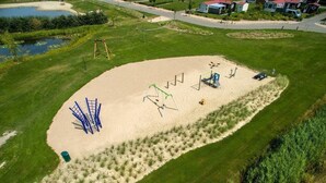 An aerial view of a park with a sandy play area, walking paths, and a pond. - Chalet Florence 5 , 6- Persoons met Veel Privacy; Huisdiervrij,ruime Tuin (Serooskerke)