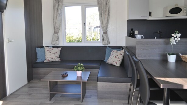 A modern kitchen with a built-in microwave, a dining table, and a seating area with cushions. - Chalet Florence 5 , 6- Persoons met Veel Privacy; Huisdiervrij,ruime Tuin (Serooskerke)