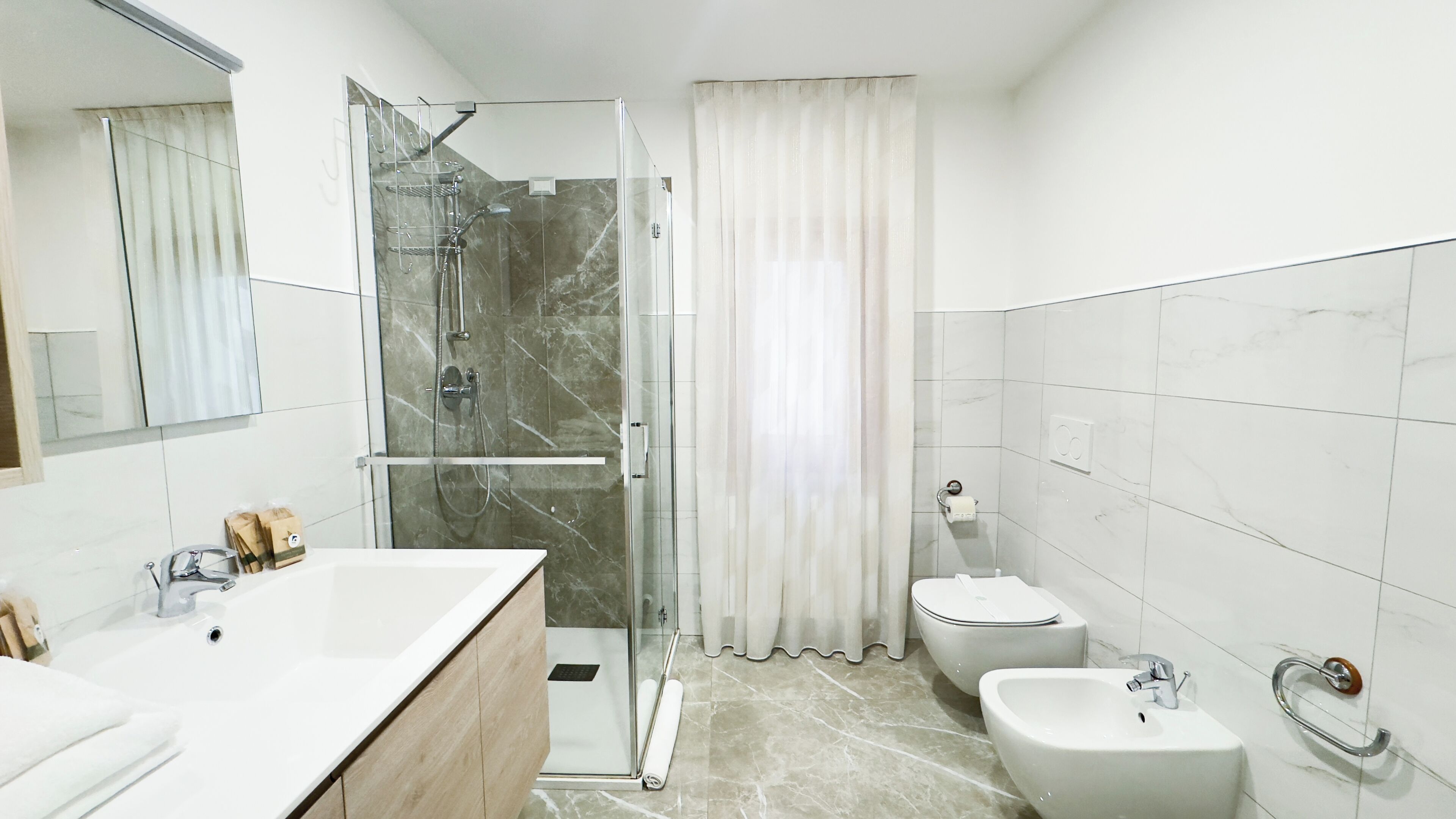 A modern bathroom with a glass-enclosed shower, a large white sink, a bidet, and a vanity with a mirror.