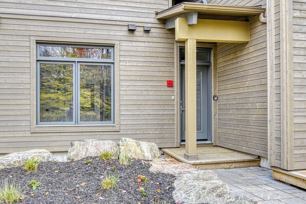 A modern building with a wooden exterior, a large window, and a small porch area.