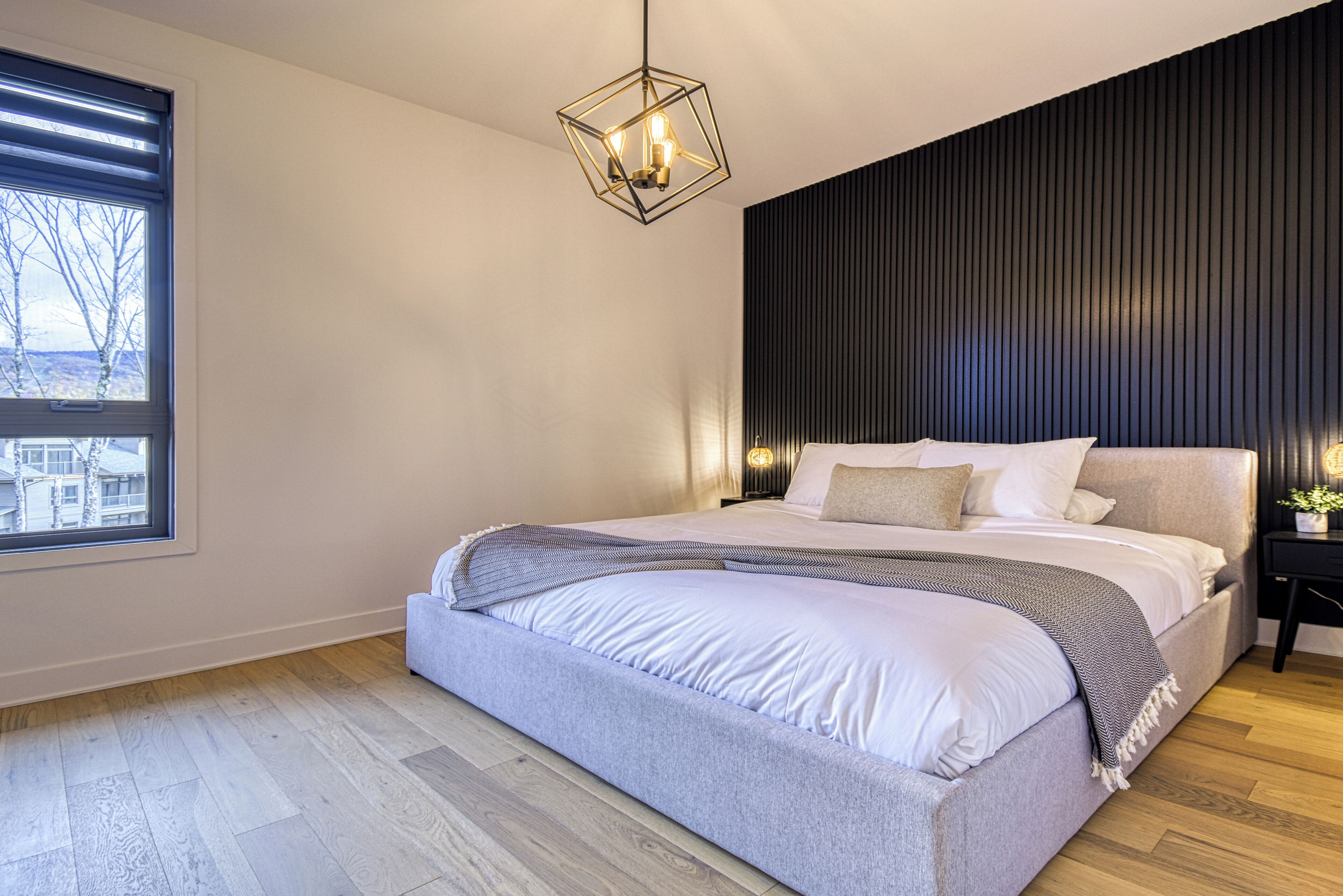 Ein modernes Schlafzimmer mit einem großen Bett, einem Fenster mit Jalousien, einem geometrischen Lichtarmaturen und einer dunklen Akzentwand.
