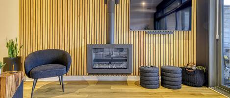 A modern living room with a wood-paneled wall, a fireplace, a comfortable chair, and a small table with a plant.