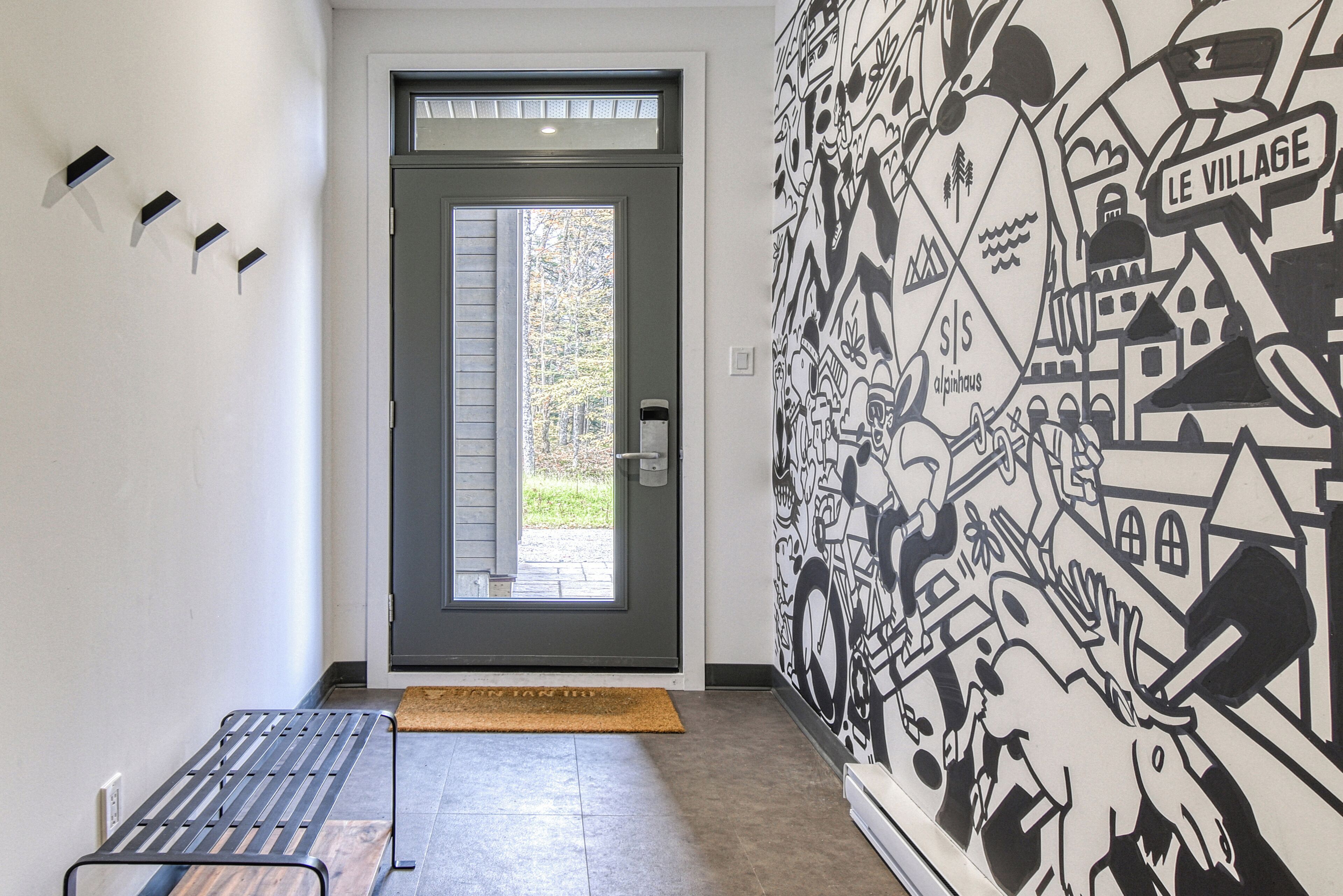 Una entrada moderna con una puerta gris, un mural blanco y negro y un banco.