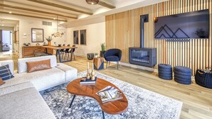 A modern living room with a fireplace, wooden panel wall, and a large TV. - 102 Verbier Building 7 - Alpinhaus (Mont-Tremblant)