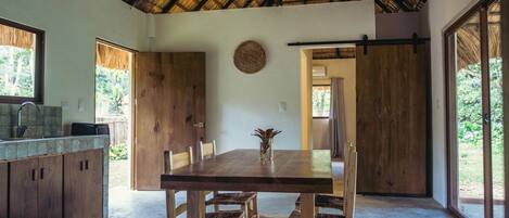 A spacious dining area with a large wooden table and chairs, a kitchen area with wooden cabinets, and large windows offering views of the outdoors.