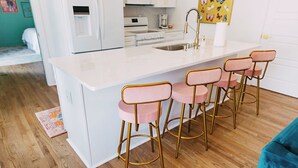 A kitchen with a white island, four pink bar stools, a blue couch, and a wooden floor. - NEW!! Forever Young I Pettigrew Adventures in Midtown  (Memphis)