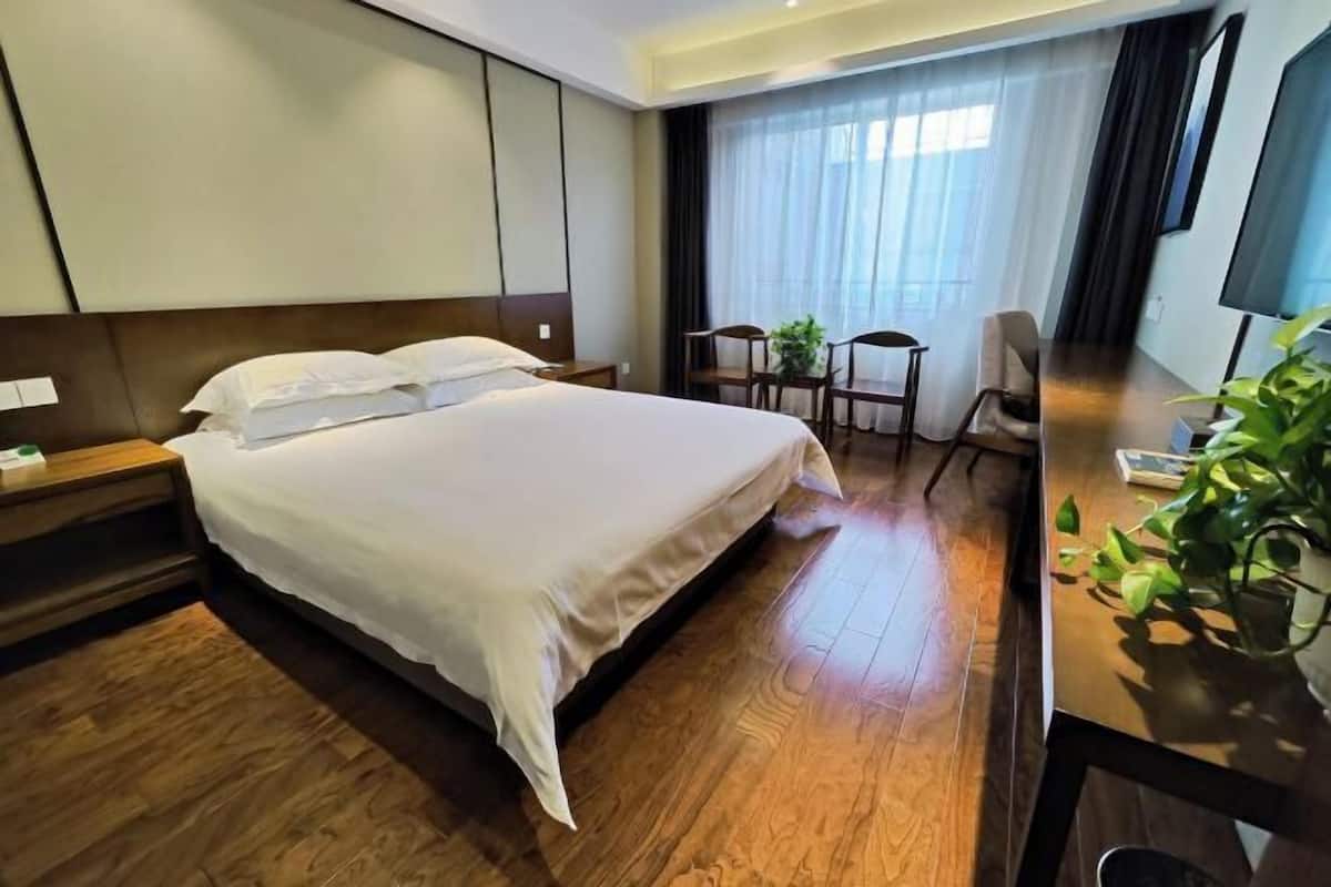 A hotel room with a large bed, a desk with a chair, a small table with chairs, and a TV.