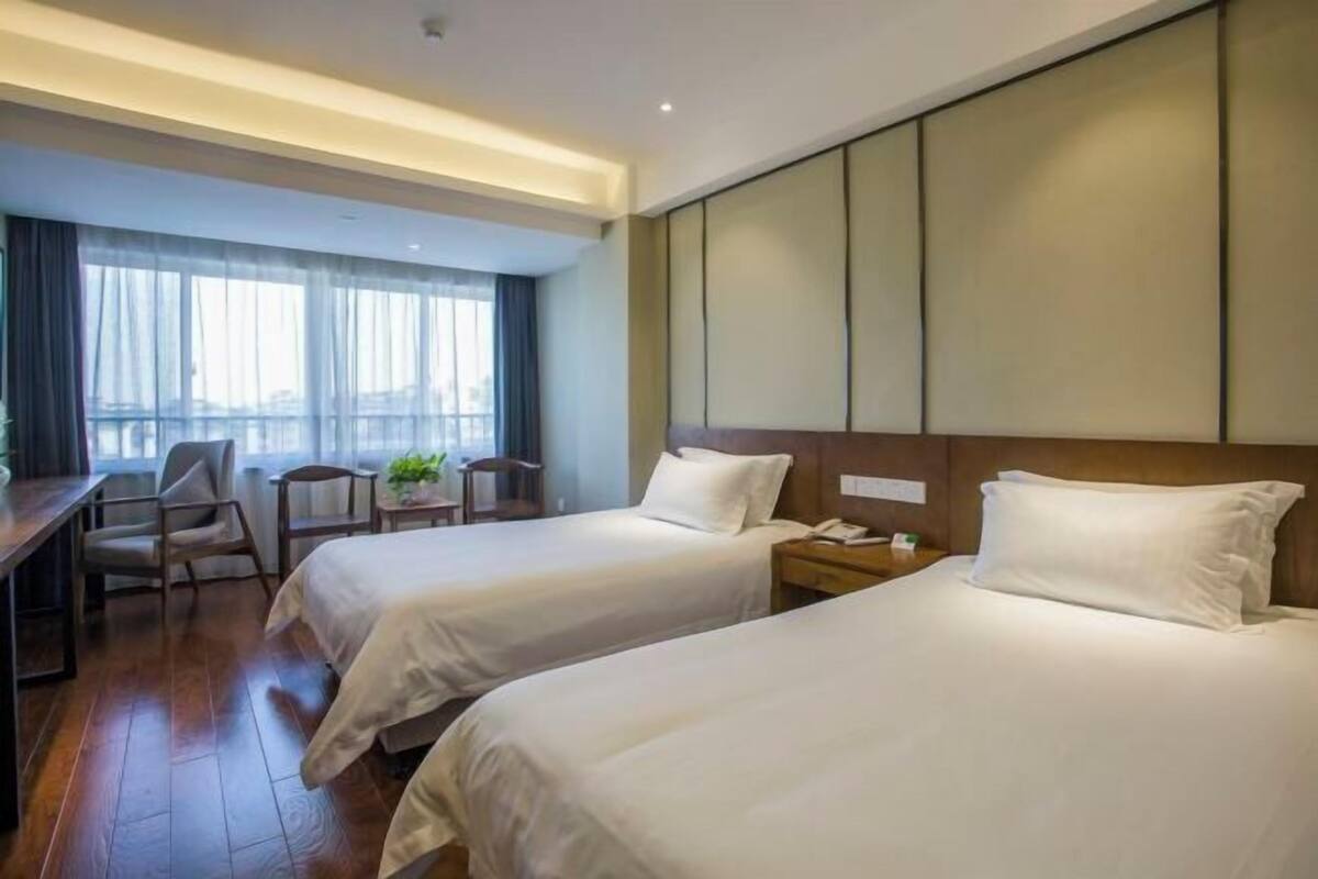 A hotel room with two beds, a desk, a chair, and a window with curtains.