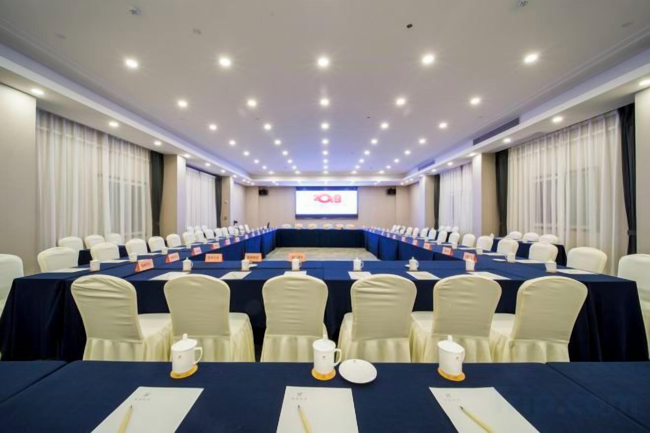 A conference room with a long table, chairs, nameplates, and a screen at the front.